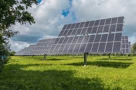 Rozległa instalacja paneli słonecznych na łące, widok z dołu, błękitne niebo z chmurami w tle.