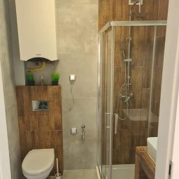 DamKar - Nowoczesna łazienka z kabiną prysznicową, wiszącą toaletą i piecem gazowym, wykończona płytkami imitującymi drewno i szarym gresem.