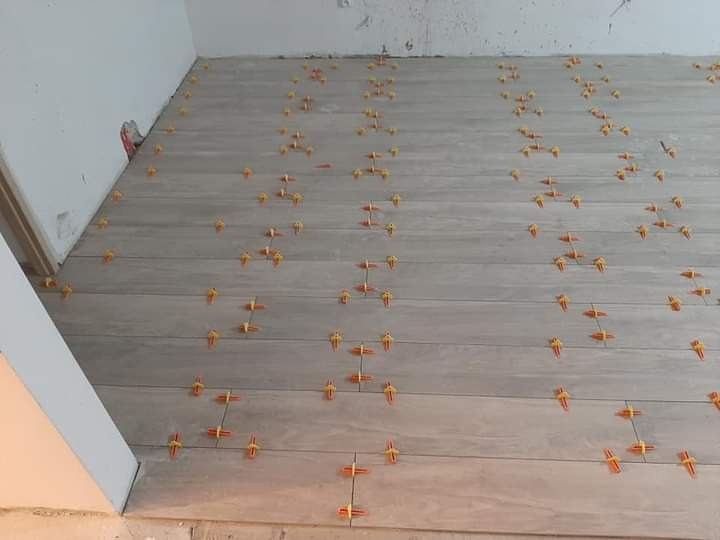 Układanie podłogi z paneli imitujących drewno, z użyciem pomarańczowych krzyżyków dystansowych, widoczne niedokończone wykończenie przy ścianie.