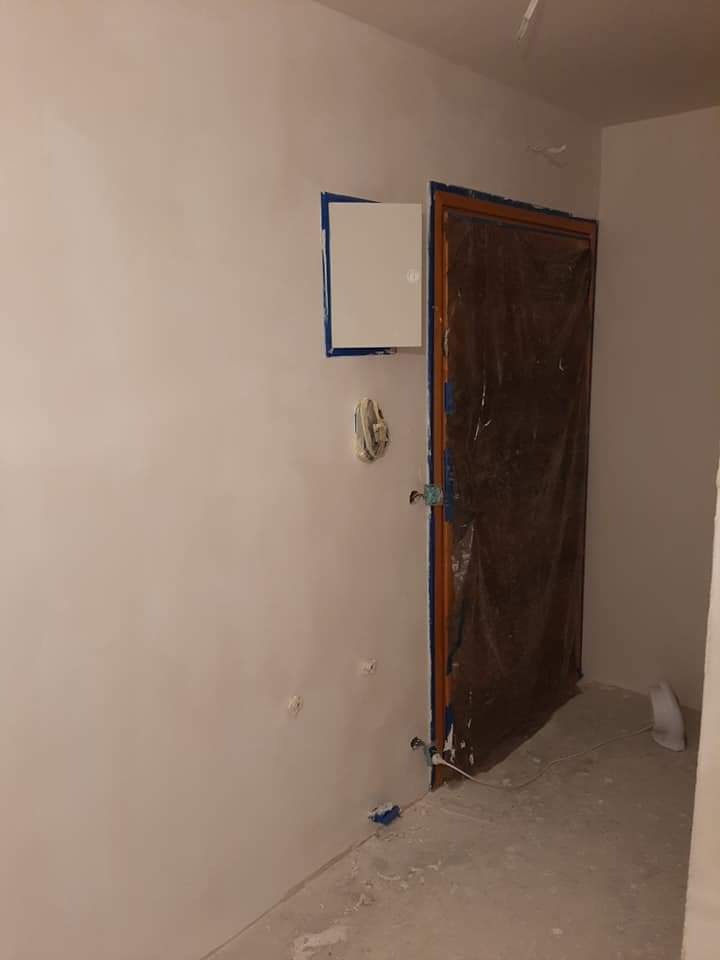 Świeżo pomalowane wnętrze pokoju z zabezpieczonymi folią drzwiami i zaklejonymi elementami na ścianie taśmą malarską, widoczne ślady po gipsowaniu i szpachlowaniu na ścianach i podłodze.