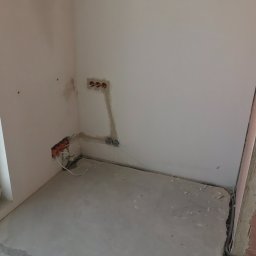 Crado - Przygotowanie ściany pod gładzie: widoczne puszki elektryczne i przewody w bruzdach, ściana zagruntowana, surowy mur z boku.