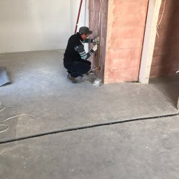 Crado - Elektryk w Regułach instaluje przewody elektryczne w nowo wzniesionej ścianie z czerwonej cegły, widoczne przewody i puszki elektryczne.