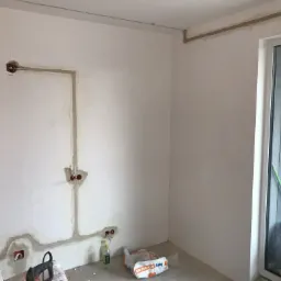 Ściana w trakcie przygotowania do malowania w Regułach, z widocznymi śladami po szpachlowaniu wok&oacute;ł puszek elektrycznych i bruzd po przewodach.