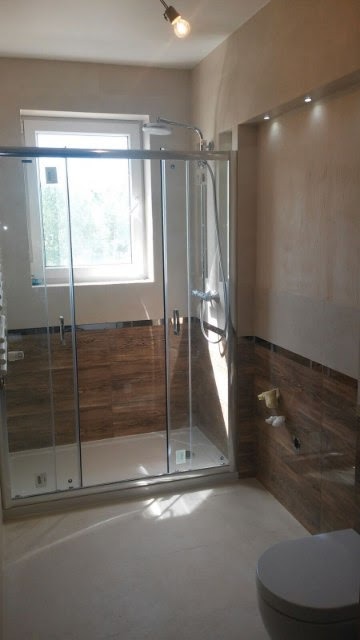 Wykończona łazienka z kabiną prysznicową ze szklanymi drzwiami, drewnopodobnymi płytkami na ścianach i podświetlanym sufitem wnękowym.