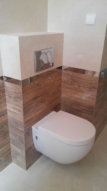 Zawieszona toaleta z zabudową w odcieniach beżu i brązu, z chromowanymi akcentami, widoczny przycisk spłukiwania i włącznik światła.