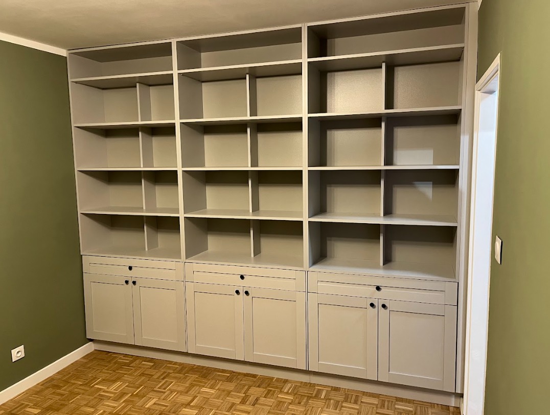 Pełna ściana zabudowana jasnoszarą szafą z półkami i szafkami na dole, widoczna na tle zielonej ściany i parkietu.