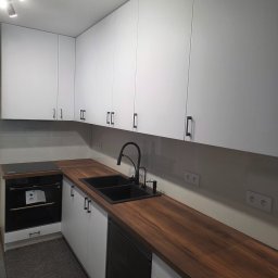 Wit-bud - Nowoczesna kuchnia z białymi szafkami, drewnianym blatem i czarną armaturą. Minimalistyczny design, oświetlenie punktowe, gładkie fronty szafek.