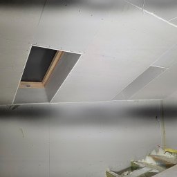 Wit-bud - Montaż płyt gipsowo-kartonowych na poddaszu z oknem dachowym. Widoczne łączenia płyt i wkręty. Częściowo ocieplone poddasze. Ujęcie z dołu.