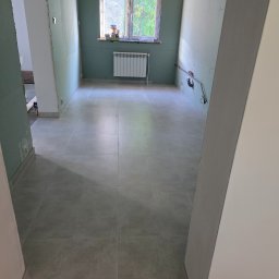 Wit-bud - Wykończona podłoga z płytek w łazience w Krakowie, ściany przygotowane pod malowanie, widoczne instalacje. Grzejnik pod oknem.