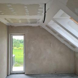 Wit-bud - Pokój na poddaszu w trakcie szpachlowania i przygotowania do malowania. Widoczne okno dachowe, ściany w szpachli i wystające przewody elektryczne.