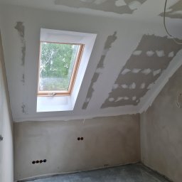 Wit-bud - Poddasze w trakcie szpachlowania z oknem dachowym. Widoczne ślady po łatach gipsowych na skośnym suficie i ścianach. Surowy stan wykończenia, przygotowanie do malowania.