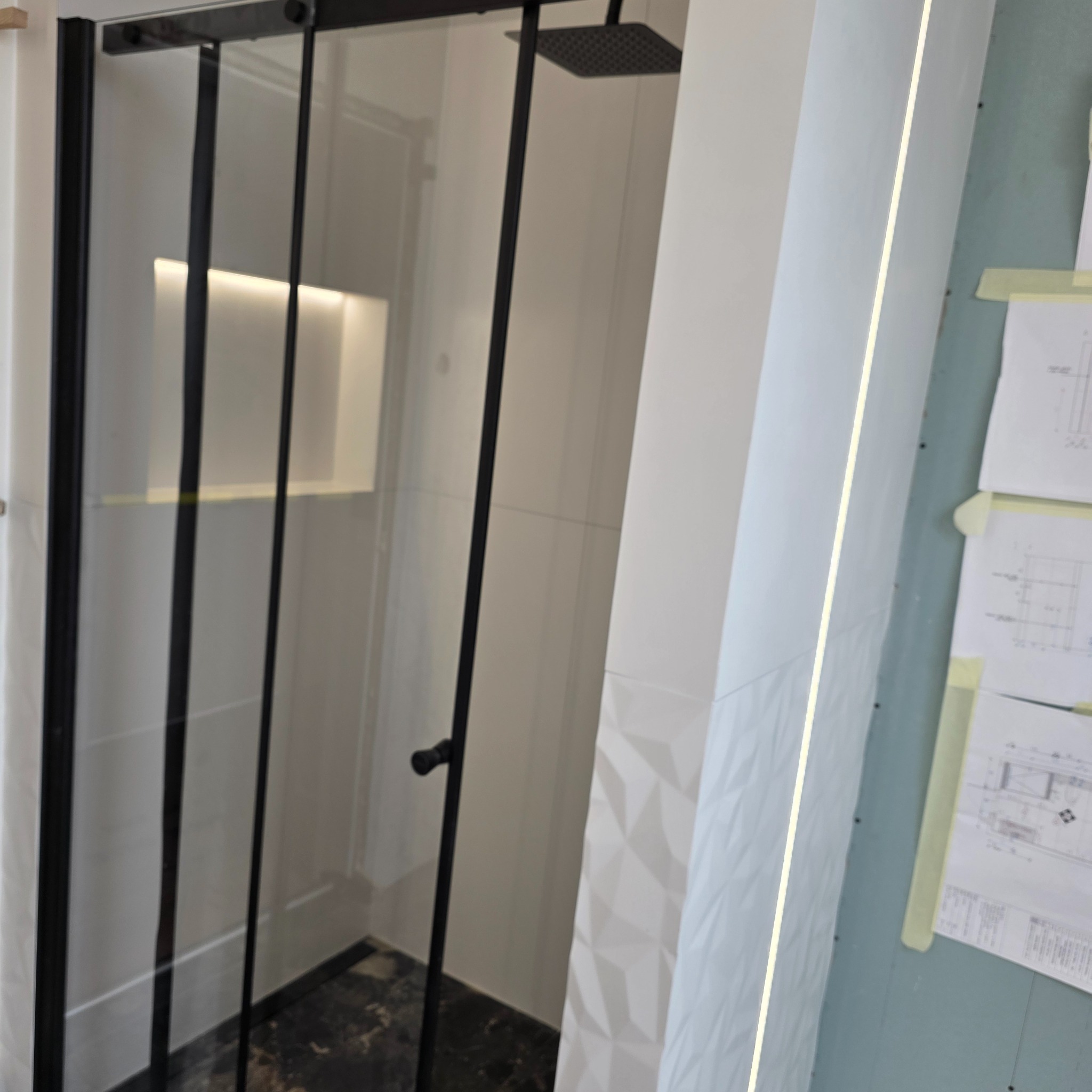 Nowoczesna kabina prysznicowa z czarnymi profilami w łazience w Krakowie. Widoczna geometryczna ściana i dokumentacja projektowa.