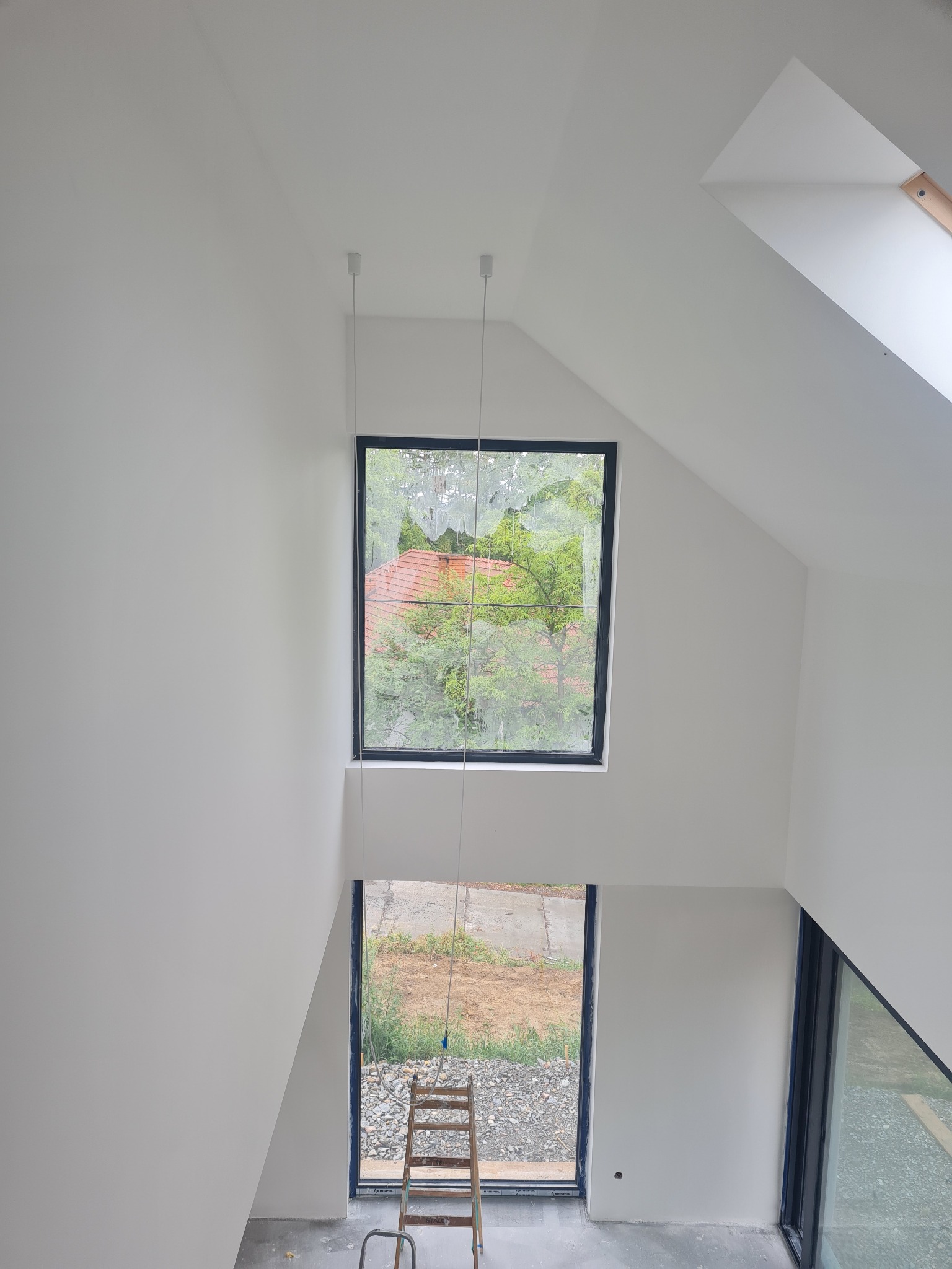 Białe wnętrze ze schodami i oknami, widok z góry. Świeżo pomalowane ściany, drabina przy oknie. Minimalistyczny design, surowe wykończenie poddasza.