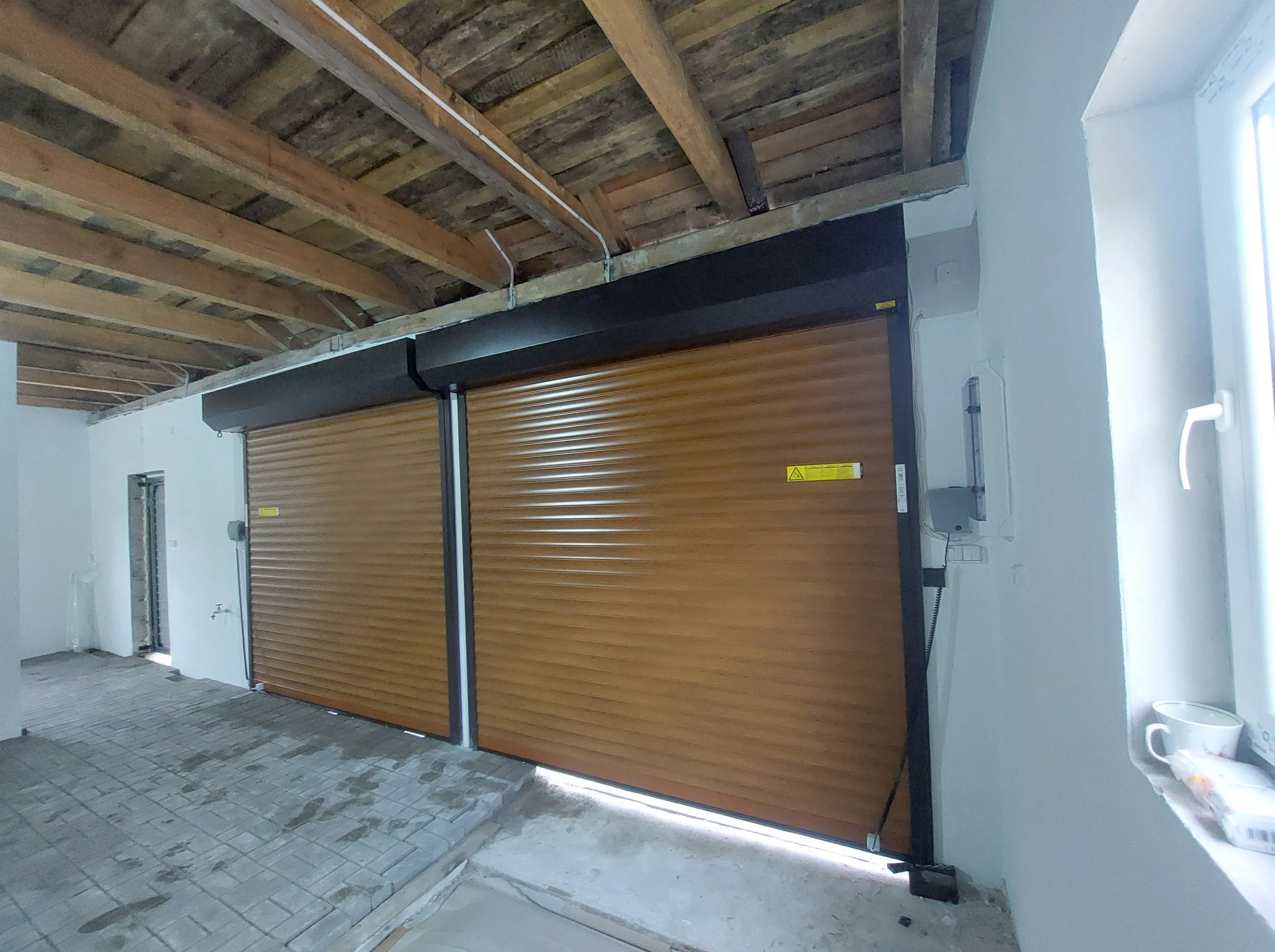 Brązowe rolety zewnętrzne zamontowane w garażu w Świeciu, widoczne niedociągnięcia wykończeniowe ścian i sufitu.