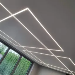 Geometryczny wzór z liniowego oświetlenia LED na suficie podwieszanym w nowoczesnym salonie z dużym oknem.