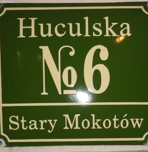 Zielona tabliczka z adresem 'Huculska No 6, Stary Mokotów' w kremowych literach, przymocowana śrubami.