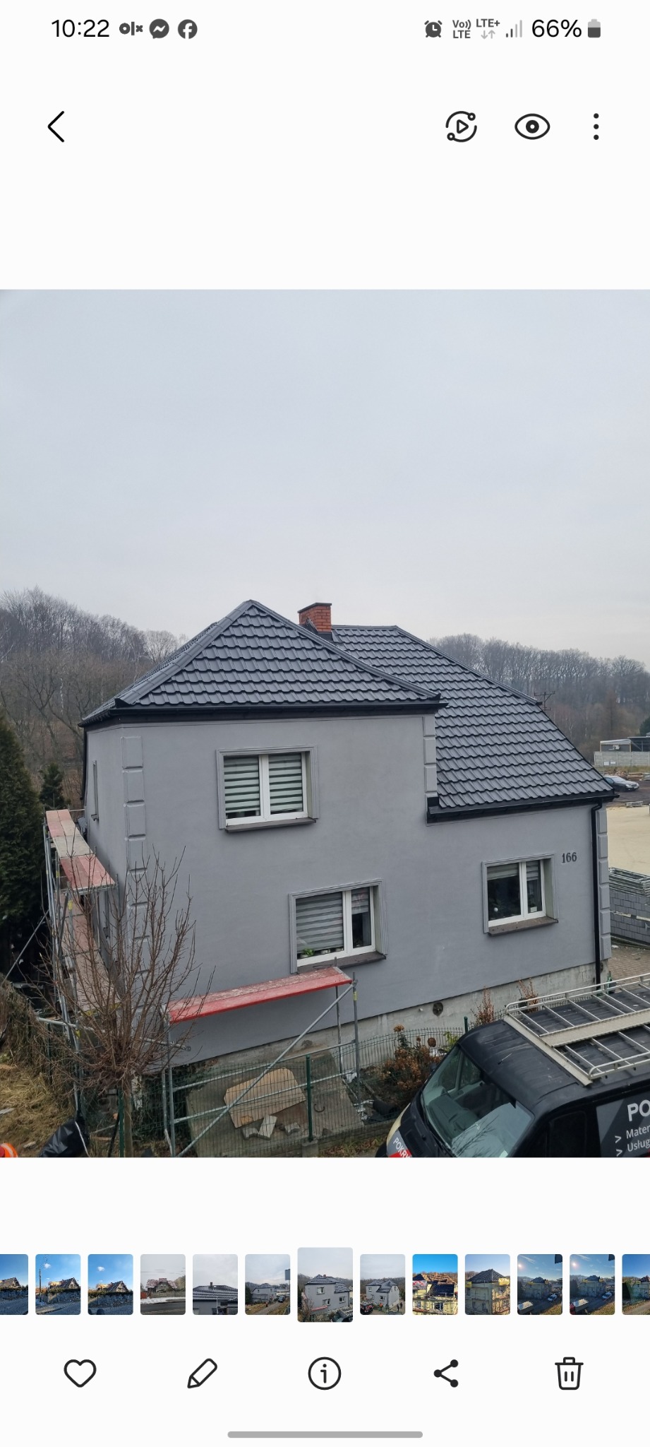 Szary dom jednorodzinny z ciemnoszarą dachówką, widziany z boku, z częściowo widocznym rusztowaniem i samochodem dostawczym firmy dekarskiej. Numer domu 166.