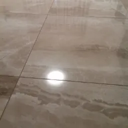 Polerowana, beżowa podłoga z płytek imitujących marmur, z widocznym odbiciem światła.