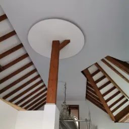 Wnętrze z drewnianą konstrukcją dachu, drewnianym słupem podtrzymującym okrągły element sufitu i widocznym rusztowaniem.