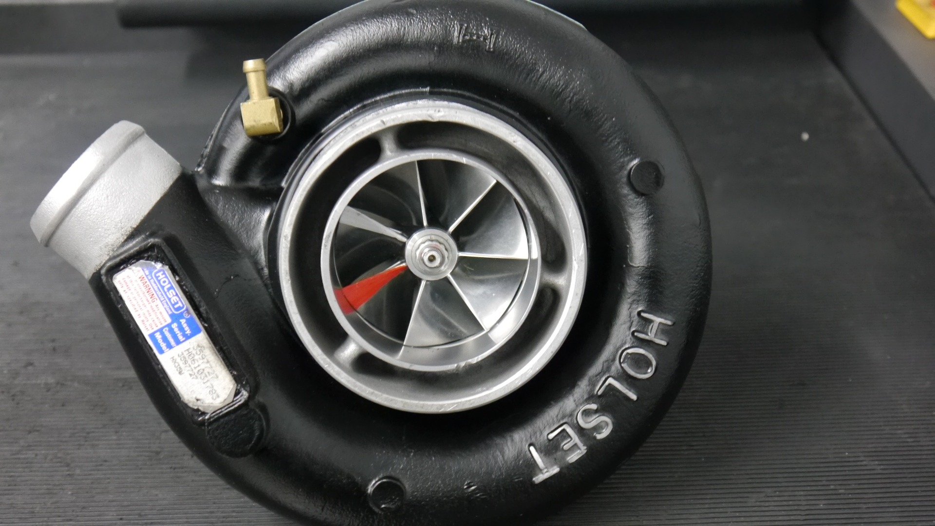 Czarna turbosprężarka Holset z widocznymi srebrnymi łopatkami wirnika i tabliczką znamionową.