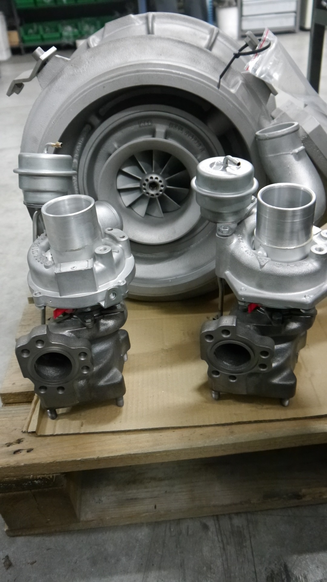 Dwa nowe, srebrne turbosprężarki na palecie, z większą turbiną w tle, gotowe do montażu.