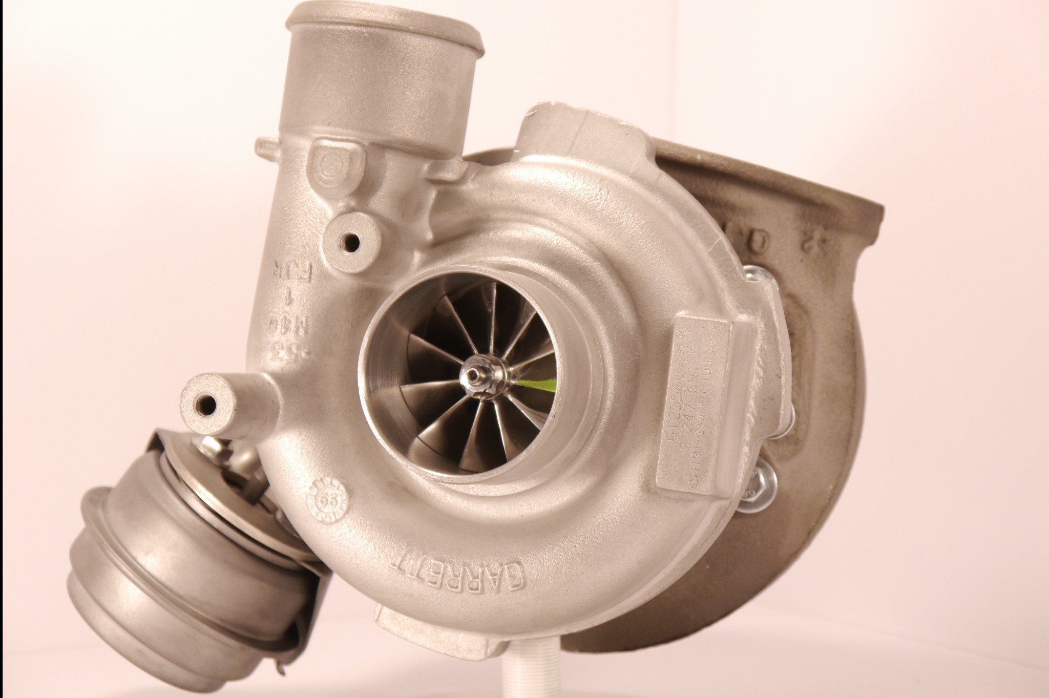 Szczegółowe ujęcie turbosprężarki marki Garrett, eksponujące aluminiową obudowę, wirnik oraz zawór upustowy, ustawionej na białym tle.