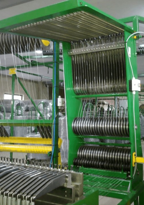 Zielona maszyna do produkcji siatki z drutu, widoczne szpule z drutem i elementy konstrukcyjne.