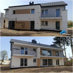 Dwukondygnacyjny dom z szarą blachodachówką, częściowo ocieplony, z elementami dekoracyjnymi imitującymi drewno na elewacji, balkony z balustradami ze stali nierdzewnej, teren wokół domu w trakcie...