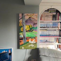 Infra-ogrzewanie - Obraz na płótnie wiszący na szarej ścianie, przedstawiający scenę z drzewem, postaciami i krajobrazem w stylu Gauguina, z widocznymi kablami zasilającymi i fragmentem regału z książkami w tle.