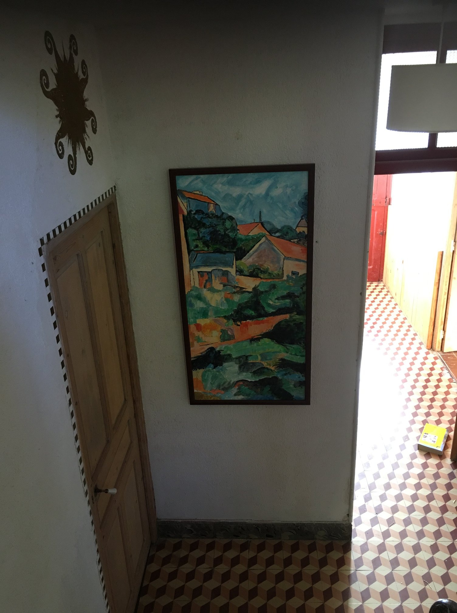 Korytarz w domu z wzorzystą podłogą, obrazem na ścianie przedstawiającym pejzaż i drewnianymi drzwiami z czarno-białymi paskami na framudze.