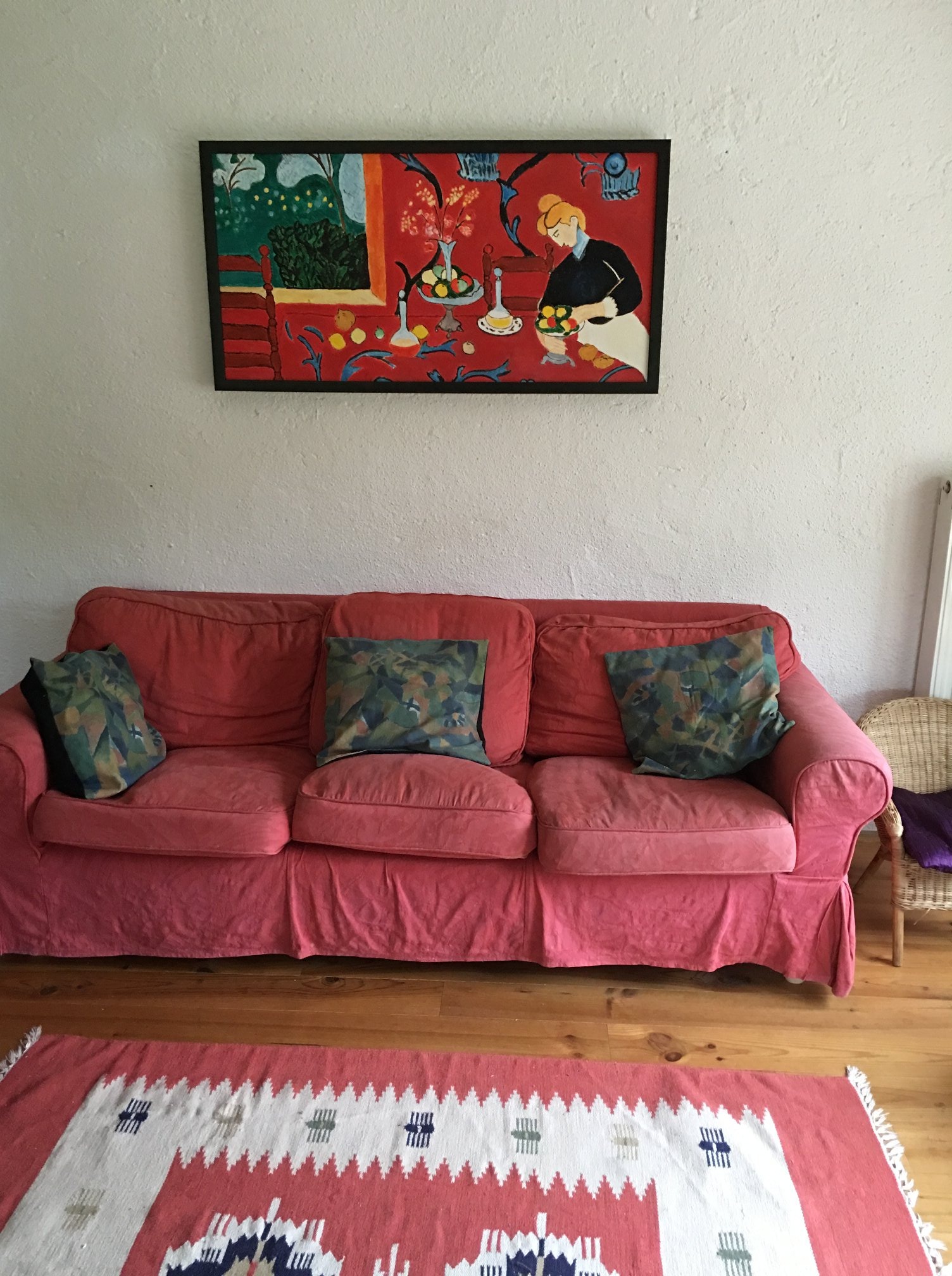 Salon z koralową sofą, poduszkami w motywy roślinne, wzorzystym dywanem i obrazem w stylu Matisse'a na ścianie.