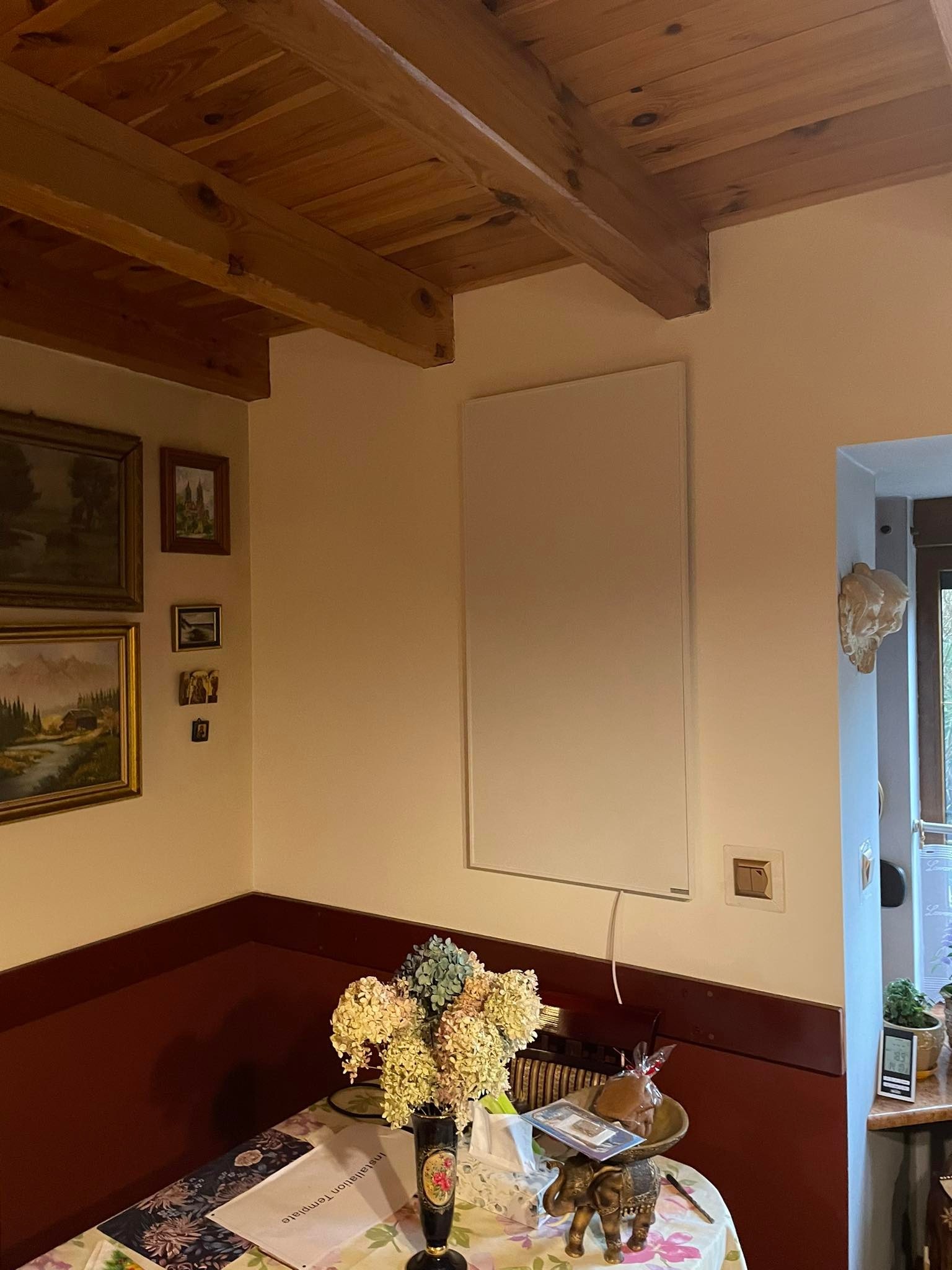 Biały panel grzewczy na ścianie w pokoju z drewnianym sufitem, dekoracjami i kwiatami na stole.