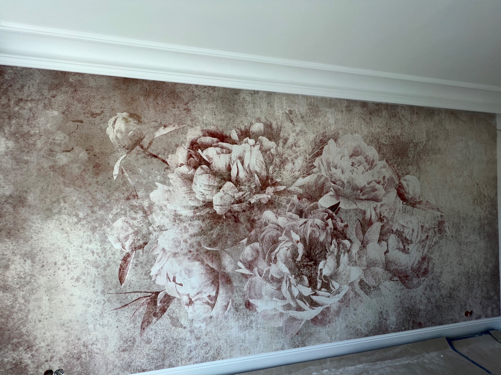 Tapeta z motywem kwiatowym w stylu vintage, z widocznymi przewodami elektrycznymi w dolnej części ściany, sugerującymi prace wykończeniowe.