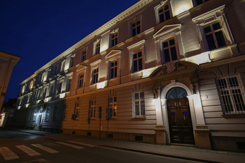 Elewacja budynku kancelarii prawnej nocą, z oświetlonym wejściem i tabliczką nad drzwiami.