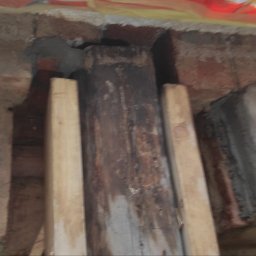 Usługi PSSN - Wzmocnienie drewnianego słupa w murze ceglanym, podpartego drewnianymi belkami. Widoczne ślady naprawy i zaprawy murarskiej. Ujęcie z bliska, w trakcie prac.