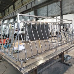 Usługi PS - Spawanie metalowej balustrady balkonowej w hali produkcyjnej. Iskry lecą spod szlifierki w rękach spawacza. Widoczne narzędzia i materiały spawalnicze.