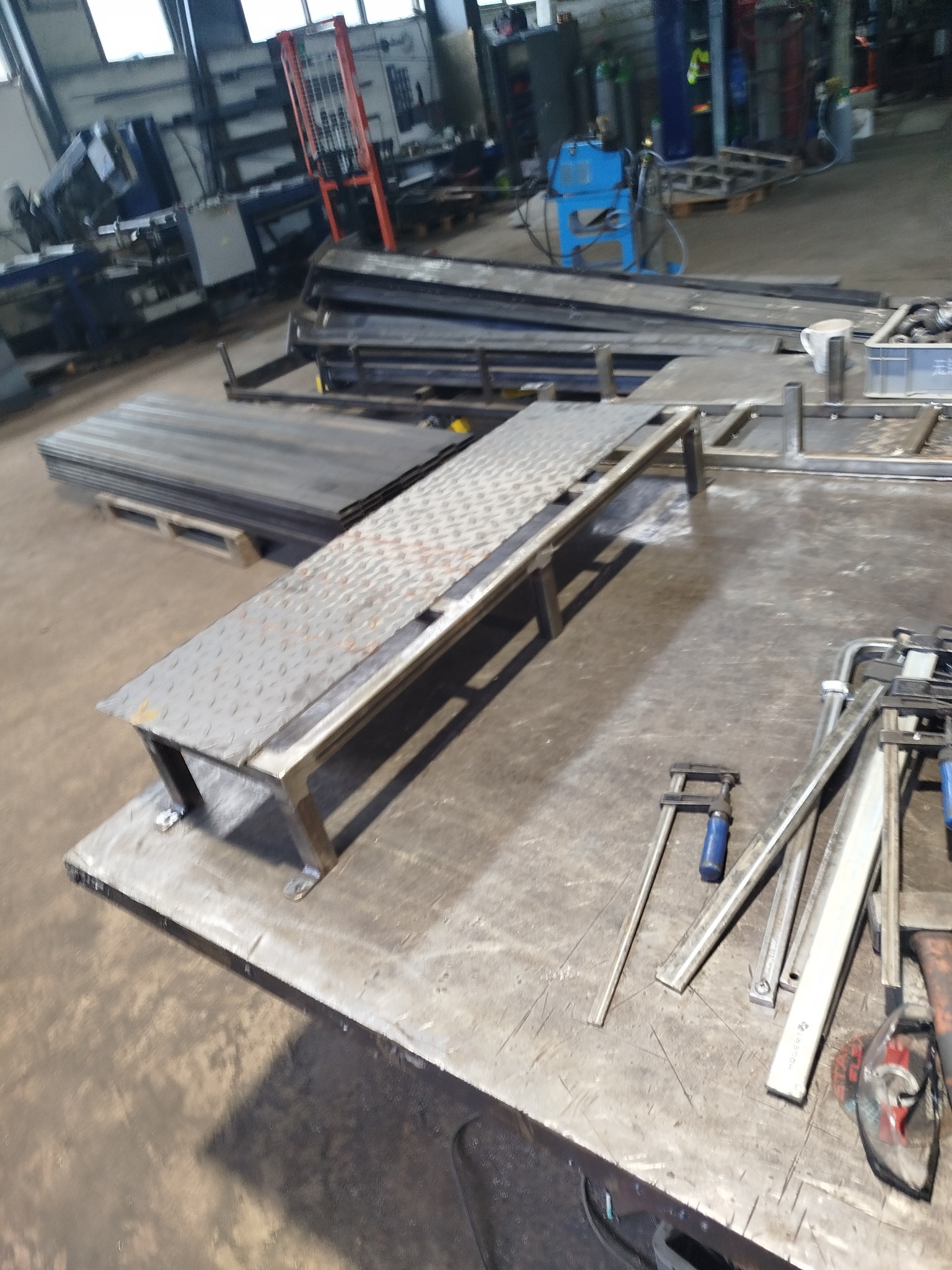 Metalowa konstrukcja z blachy ryflowanej na stole warsztatowym w hali produkcyjnej w Piławie Dolnej. Widoczne narzędzia i materiały spawalnicze w tle.