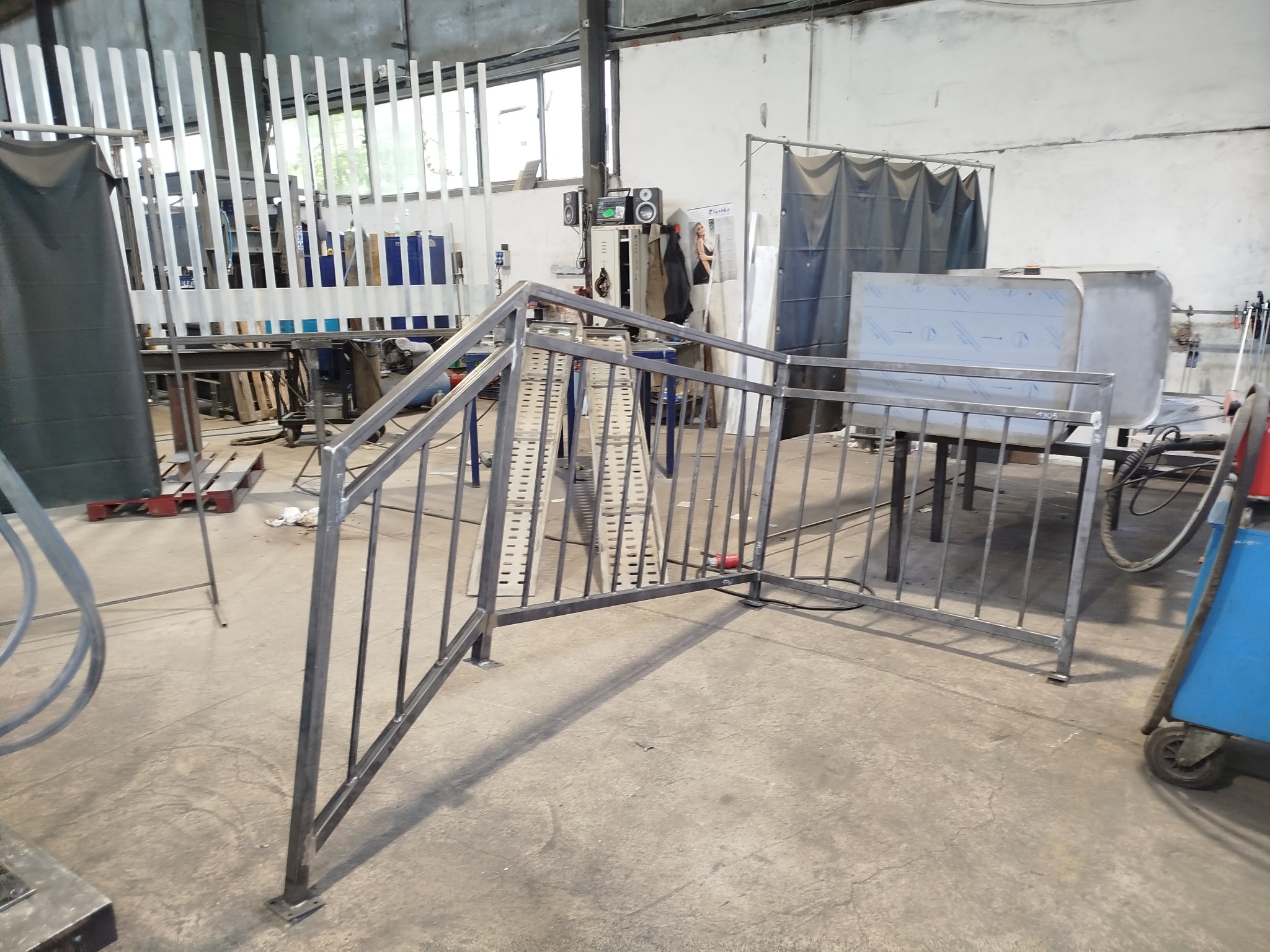 Metalowa konstrukcja balustrady schodowej w warsztacie, spawana z profili, surowa, przed malowaniem. Widoczne narzędzia i elementy wyposażenia warsztatu.