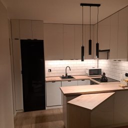 KJK Meble Krzysztof Krzysztofowicz - Nowoczesna kuchnia z białymi frontami i drewnianym blatem w Police, oświetlona wiszącymi lampami i podświetleniem LED pod szafkami, z czarną lodówką w zabudowie.