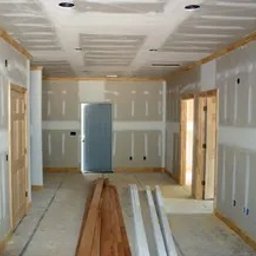 Profi - Korytarz w trakcie szpachlowania: widoczne płyty gipsowo-kartonowe na suficie i ścianach, drewniane listwy wykończeniowe, drzwi i materiały budowlane.