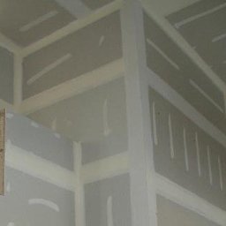 Profi - Wnętrze w trakcie prac wykończeniowych: ściany i sufit pokryte płytami gipsowo-kartonowymi, widoczny fragment ramy okiennej i rusztowania. Przygotowanie do malowania.