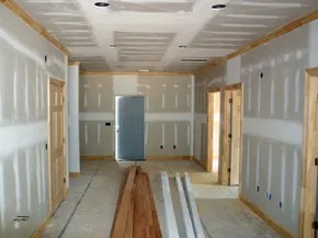 Korytarz w trakcie szpachlowania: widoczne płyty gipsowo-kartonowe na suficie i ścianach, drewniane listwy wykończeniowe, drzwi i materiały budowlane.