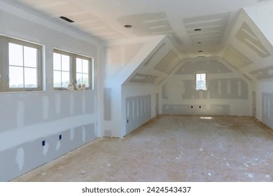 Poddasze w trakcie wykańczania: ściany i sufit pokryte szpachlą, widoczne okna i instalacje elektryczne. Przygotowanie do malowania.