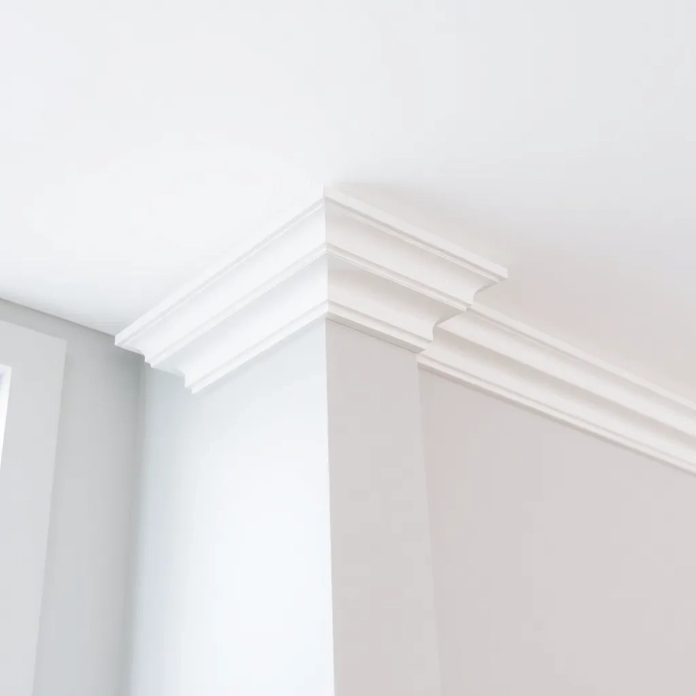 Białe, eleganckie listwy dekoracyjne zamontowane na styku ściany i sufitu w jasnym wnętrzu. Minimalistyczny design, precyzyjne wykonanie, świeżo pomalowane powierzchnie.