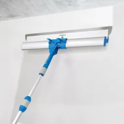 Narzędzie do rozprowadzania masy szpachlowej z teleskopową rączką marki Storch, przymocowane do białej ściany, widoczny świeżo nałożony fragment masy.