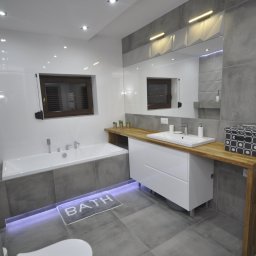 MEBLE GAL Tadeusz Gal - Nowoczesna łazienka w szaro-białej kolorystyce z drewnianym blatem, podświetlaną wanną i minimalistycznym grzejnikiem drabinkowym.