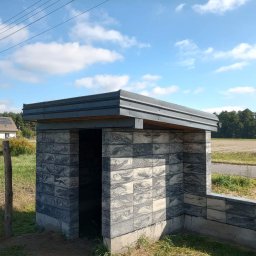 Jurex - Murowana, otwarta altana z bloków betonowych o szarej, marmurkowej fakturze, z metalowym zadaszeniem, na tle pola i błękitnego nieba z chmurami.