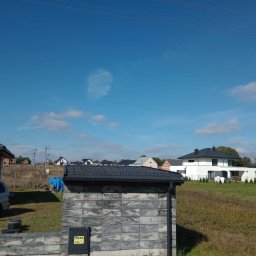 Jurex - Nowoczesny dom jednorodzinny z czarną dachówką ceramiczną, widok z poziomu gruntu na tle błękitnego nieba z lekkimi obłokami.