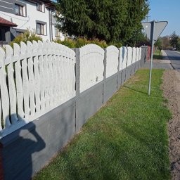 Jurex - Nowoczesne ogrodzenie betonowe z dekoracyjnymi przęsłami w kolorze białym i szarą podmurówką, zakończone ceglanym słupkiem, oddzielające posesję od ulicy.
