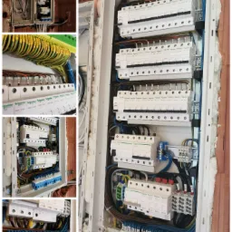 Rozdzielnica elektryczna w trakcie montażu, widoczne zabezpieczenia różnicowoprądowe, bezpieczniki, listwy zaciskowe z opisami przewodów, instalacja w surowym murze z cegły.